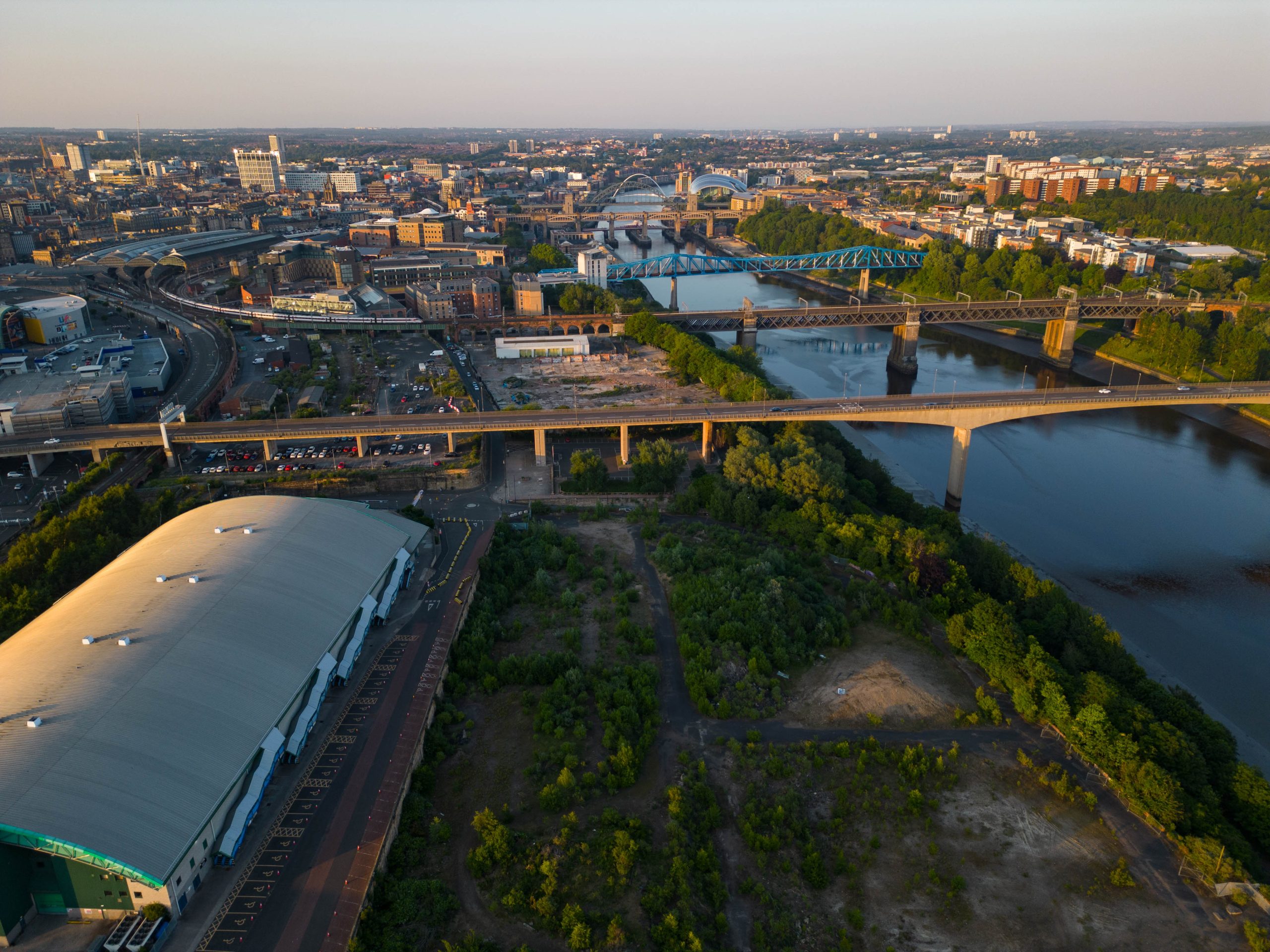 Aerial view of the Forth Yards site next to the River Tyne, there is a large arena to the bottom left and lots of brownfield across the rest of the site.