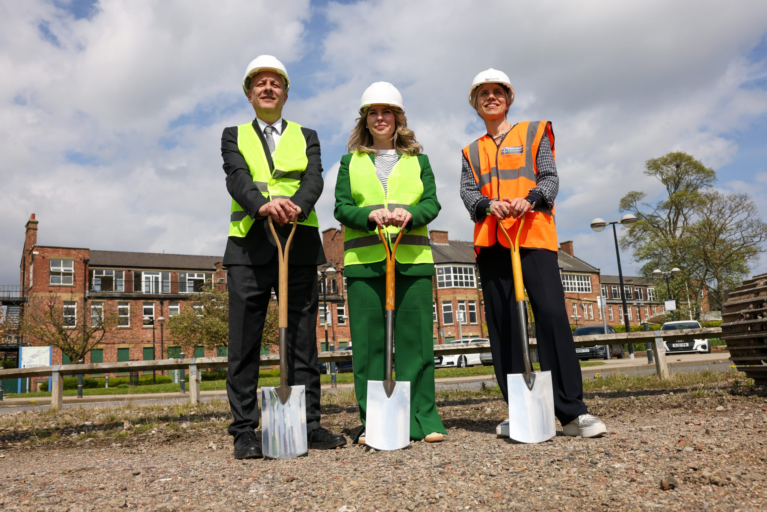 Three people wearing high visibility gear and pushing shovels into the soil