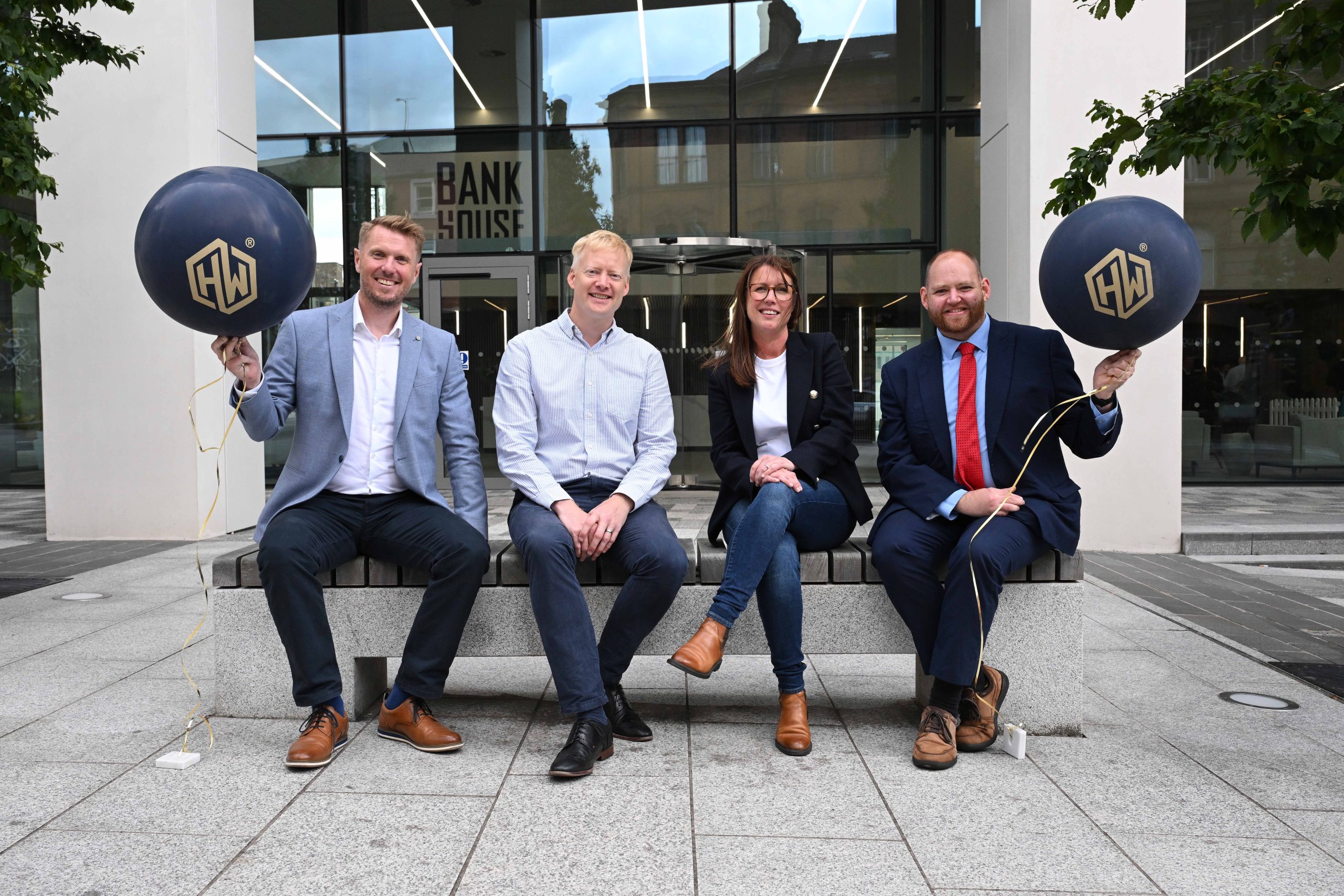 Group of four people outside of office building holding Hagen Wolf balloons.