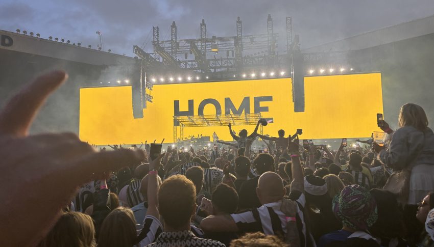 Gig-goers watching on at Sam Fender on stage with the big screen on the background with HOME in black letters written across the stage.