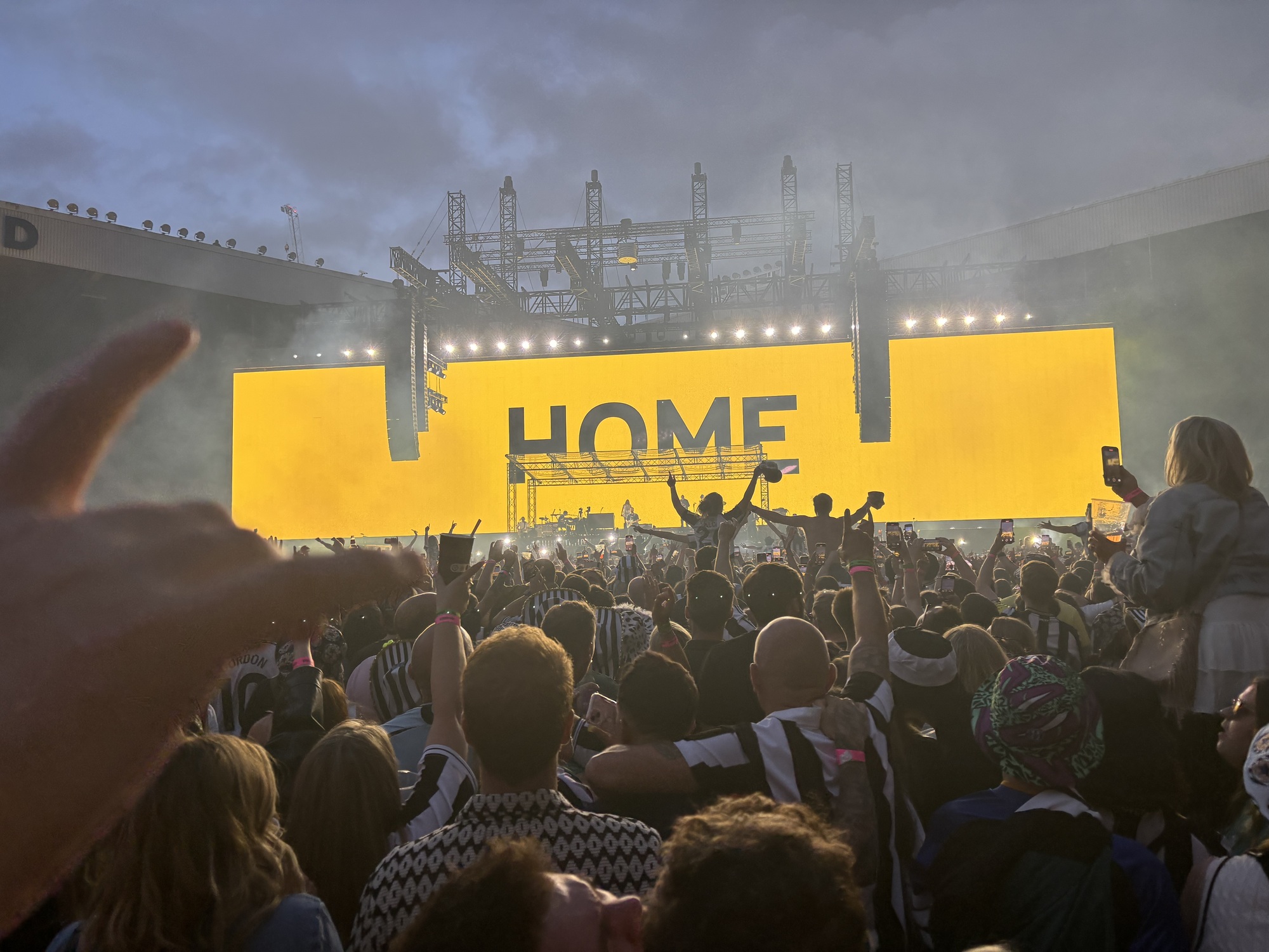 Gig-goers watching on at Sam Fender on stage with the big screen on the background with HOME in black letters written across the stage.