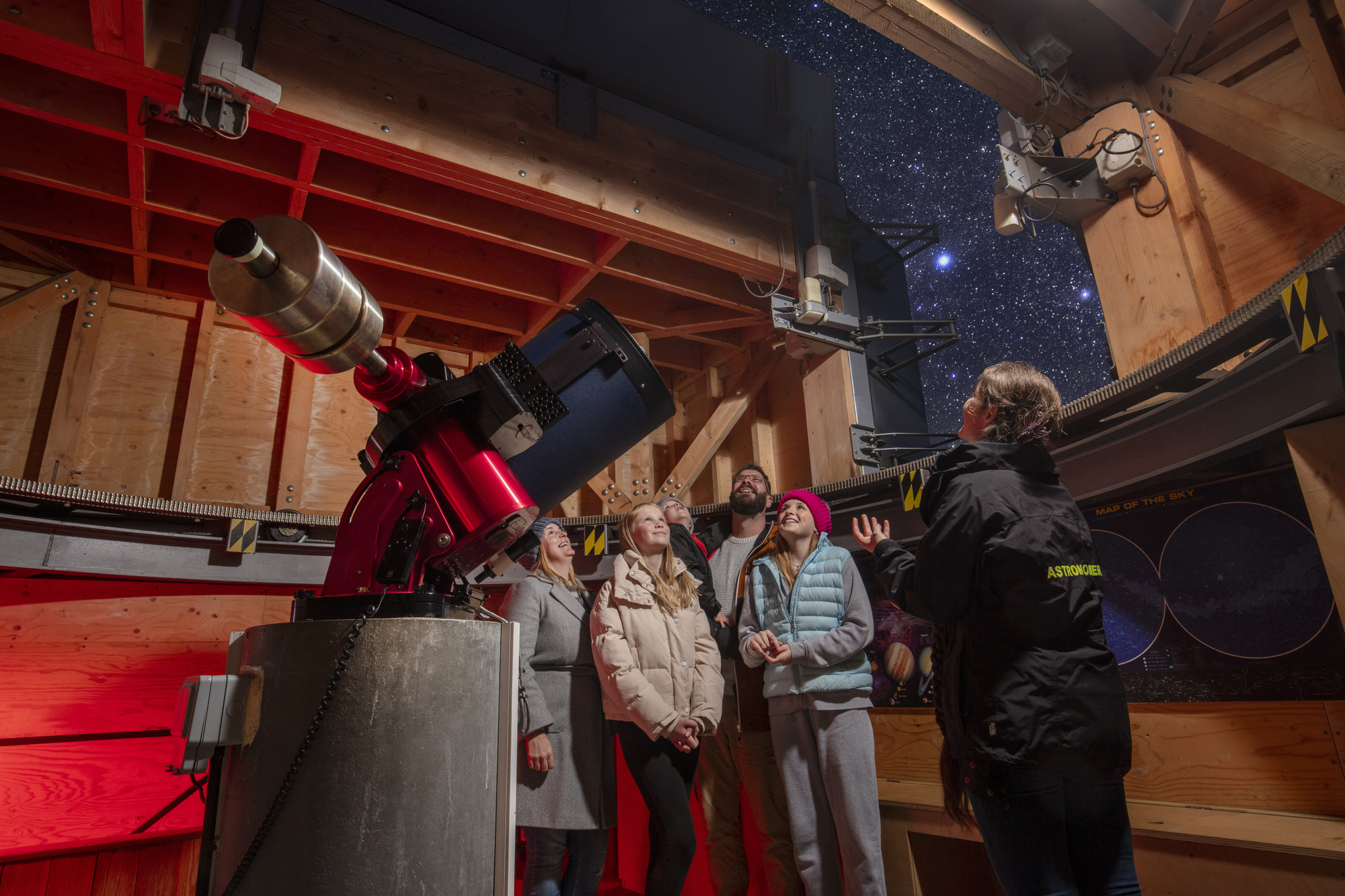 A family of five, one male adult one female adult one boy and two girls winter dressed listening to a female astronomer Kielder Observatory